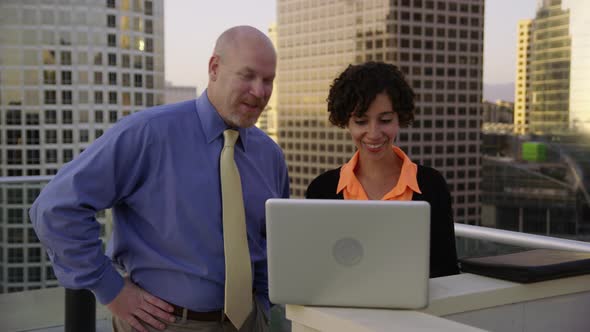 Businesspeople outdoors on rooftop look at laptop computer together