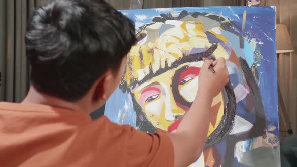 Hind View Of An Asian Artist Boy In Wheelchair Painting A Girl's Face On The Canvas alt