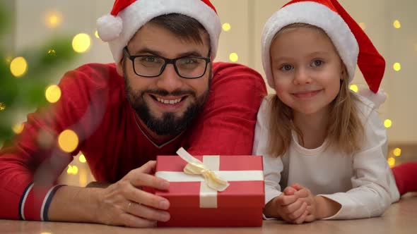 Father and Girl with Gifts Look at Camera Smile and Laugh Next to Christmas Tree