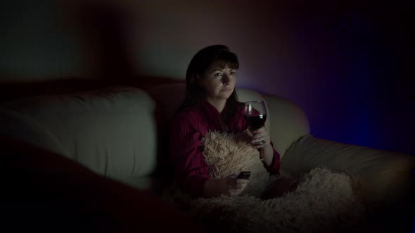 Brunette Woman Relax at Home with a Glass of Wine on the Sofa and Watches Tv at Night
