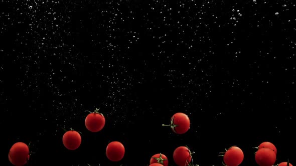 Red Cherry Tomatoes Falling Into Water with Air Bubbles Black Background alt