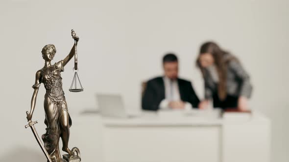 Statue of Justice on the background of two people who work with documents