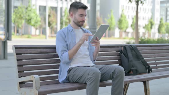 Young Man Using Tablet While Sitting on Bench alt