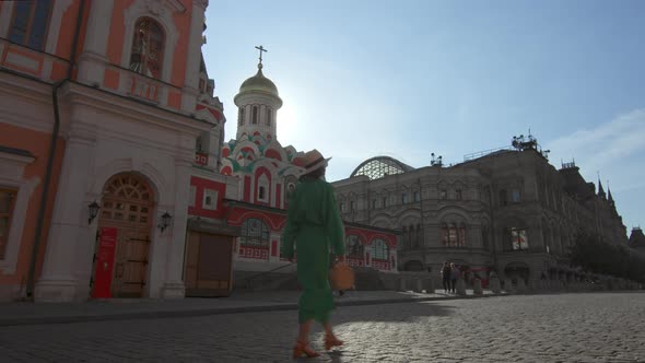 A girl in a green dress walking by the cathedral on Red Square alt
