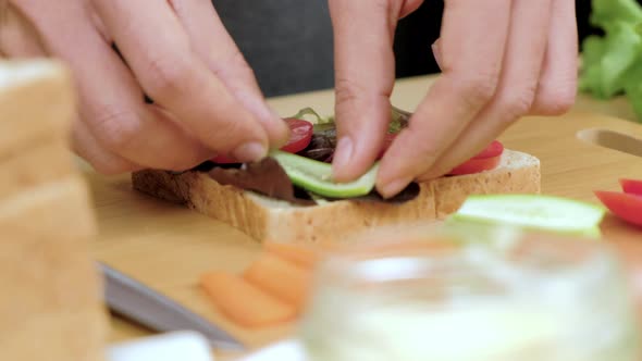 Woman's hands put fresh cucumber slice on healthy sandwich, Close up.