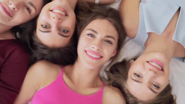 Top View of Stunning Women Lying Head To Head on Big Bed alt