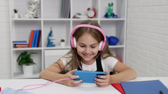 Happy Kid in Headphones Watching Video on Mobile Phone in Classroom Video Call