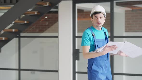 Handsome Young Concentrated Caucasian Builder Walking with Drawings in New Premises and Leaving alt