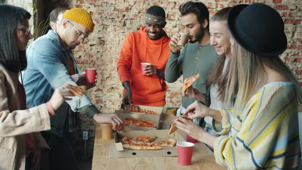 Multiethnic Group of Businesspeople Eating Pizza Together in Modern Loft Style Office alt