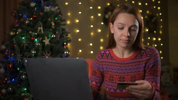 Young Woman Lying Under Christmas Tree and Ordering Gifts at Online Shop on Laptop