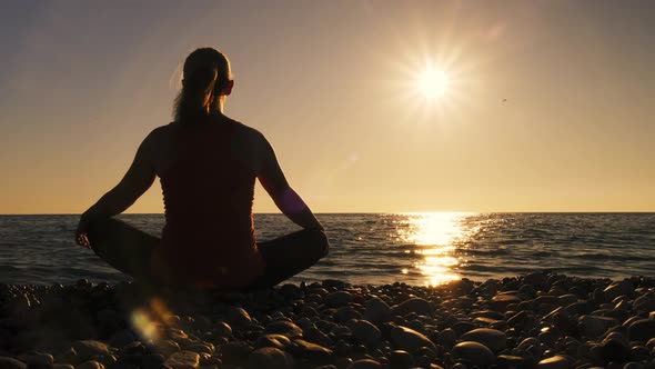 Silhouette of girl engaged in yoga sitting on seashore at sunset alt