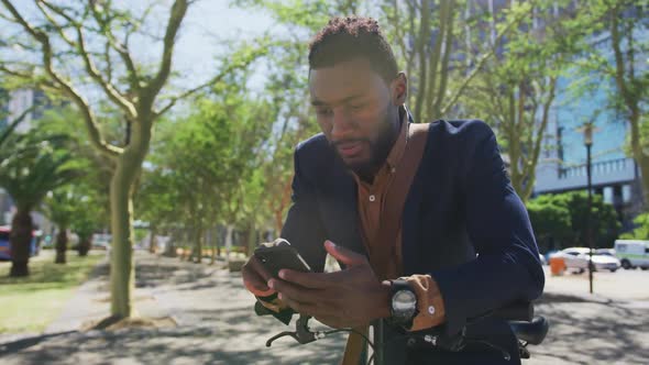 Smiling african american businessman using smartphone leaning on bike alt