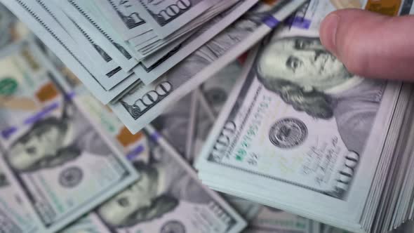 A man's hands are counting a thick stack of dollars against a background of scattered $ 100 bills. alt