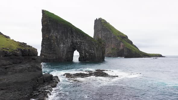 Aerial View of the Rocky Drangarnir Sea Stack in the Faroe Islands and the Skarosafossur Waterfall alt