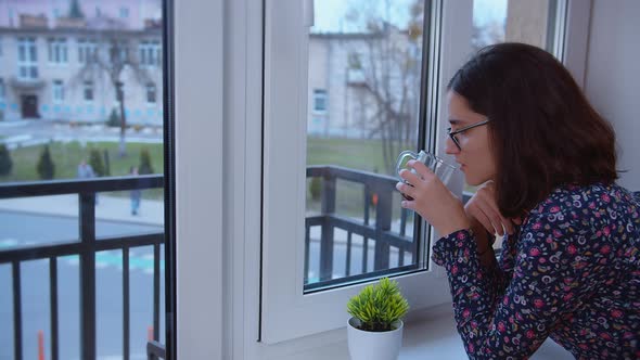 Sad Girl in Anticipation Looks Out the Window and Drinks Coffee Copyspace alt