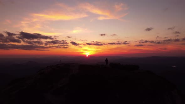 Person Standing on Rock with Epic Mountain Viewpoint with a Sunset Drone Aerial Landscape Shot