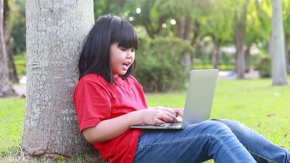a girl sitting on a computer under a tree in a public garden