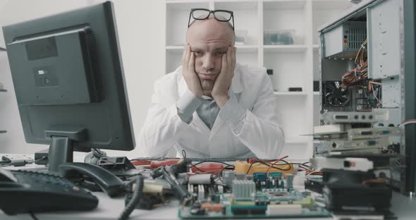 Stressed frustrated computer repair technician sitting at desk