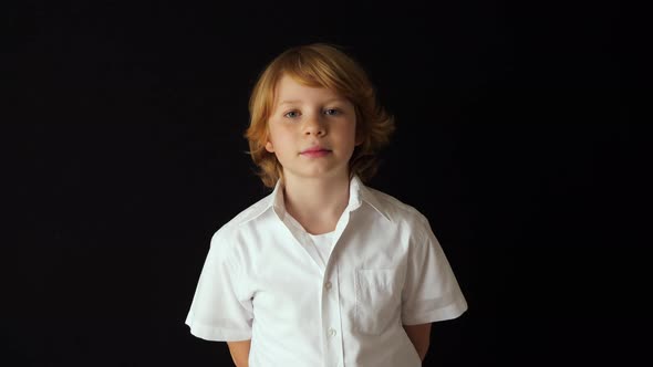 Blonde boy in white shirt stands against black background