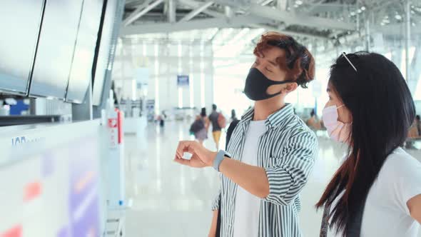 Asian male and female wearing protective face mask in airport terminal.