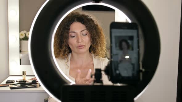Cheerful Female Vlogger is Showing Cosmetics Products While Recording Video and Giving Advices for alt