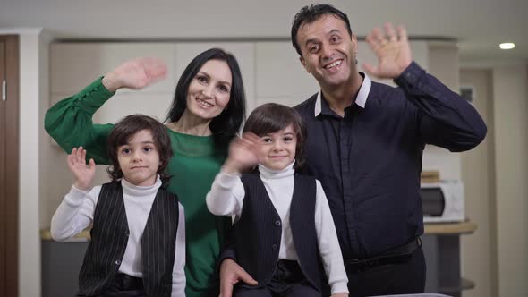 Happy Cheerful Multiethnic Family Waving Smiling Looking at Camera Indoors alt