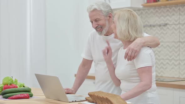 Loving Old Couple Doing Video Call on Laptop in Kitchen alt
