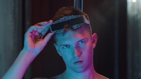 A Young Man Stripper Acting Sexy in Neon Lighting  Putting on Glasses Covered in Rhinestones alt