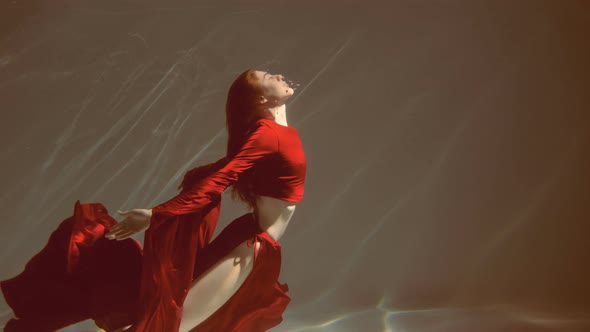 Attractive red-haired young woman swims beautifully underwater in a red dress. slow motion alt