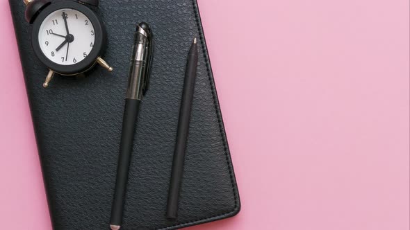 Black Notepad with a Pen and an Alarm Clock on a Pink Background alt