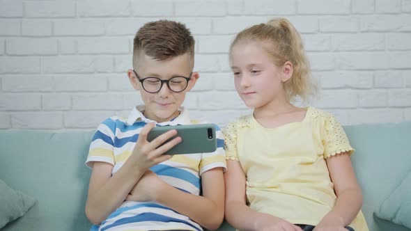 Close Up of an Excited Twins Kids Using Smartphone Sitting Together on Sofa alt