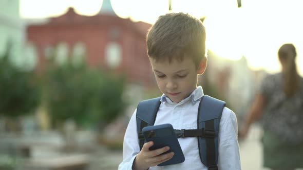Caucasian Schoolboy Surfing Internet on Smartphone Standing on the Street