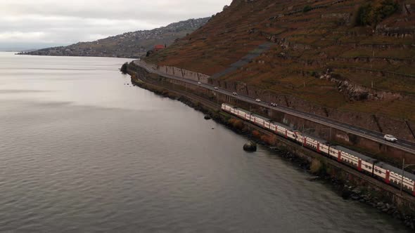 Aerial of train driving over rail track in the Swiss mountains next to lake alt