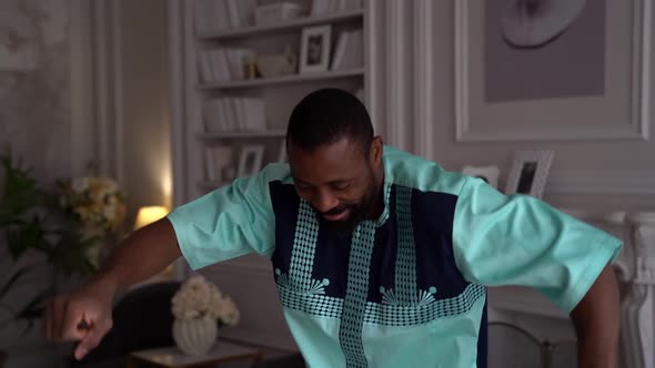 a Bearded AfricanAmerican Man in National Clothes Dances in a Living Room Against the Background of alt