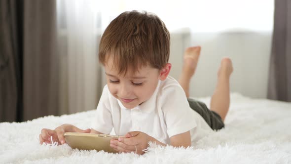 Cute Little Boy Playing Using Smartphone. The Child Looks at the Smartphone Screen and Laughs alt