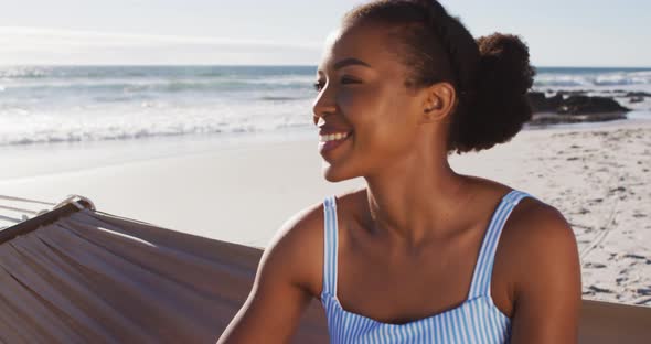 Close up of african american woman smiling while sitting on a hammock at the beach alt