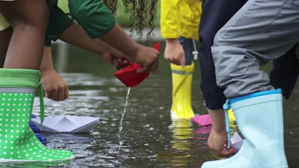 Children Putting Paper Boats in Puddle alt