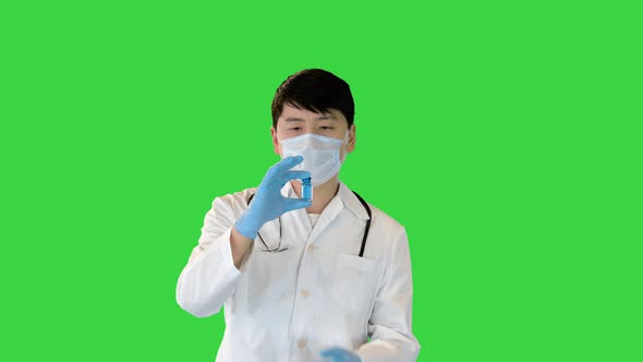 Young Asian Doctor Holding and Looking at Ampule with Blue Solution on a Green Screen Chroma Key