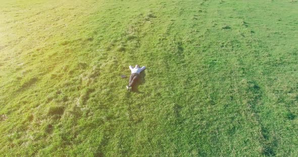Low Orbital Flight Around Man on Green Grass with Notebook Pad at Yellow Rural Field alt
