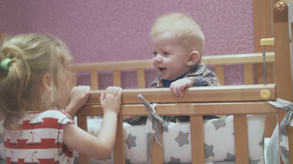 Girl Jumps Up at Cot Playing with Junior Brother in Kid Room alt