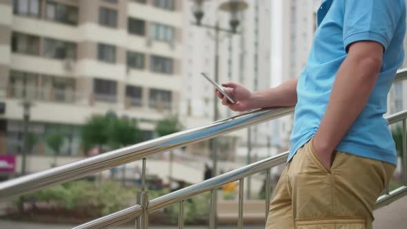 Young man in shorts with a mobile phone stands on the stairs near the railing, camera movement alt