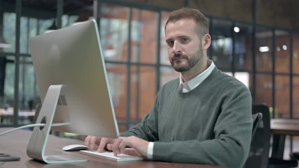 Smart Man Working on Computer and Showing Thumbs Down alt