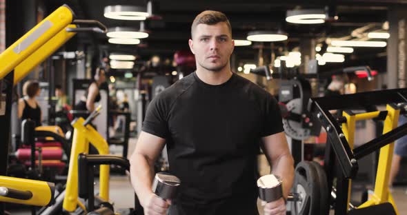 Portrait of Handsome Sportive Man in a Black Tshirt Doing Biceps Exercises in the Gym Using