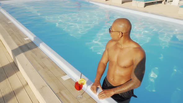 Handsome African Man Enjoying Drinking Cocktail in the Swimming Pool alt