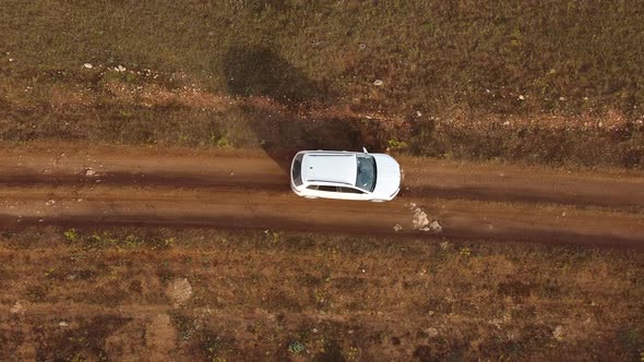 Drone Shoots From Above at a White Car Walking on a Rural Road in a Field alt