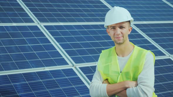 Portrait of a Worker in Overalls and a Helmet on the Background of Solar Panels. Smiles, Looks Into