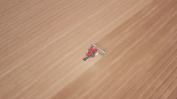 Red tractor flattening a field for seeding, Drone follow footage. alt