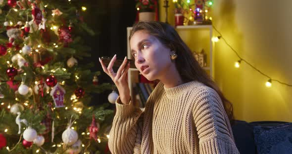 Young Woman Listening to Voice Message on Smartphone Sitting on Sofa in Living Room alt