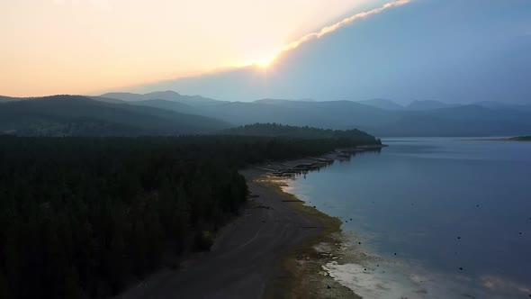 Flying backwards over lake with low water levels looking at smokey sunset alt