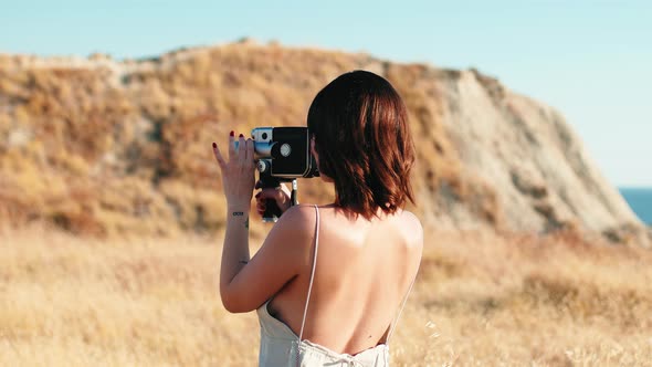 Beautiful Women Makes Shots with Vintage Camera in Yellow Countryside in Summer alt